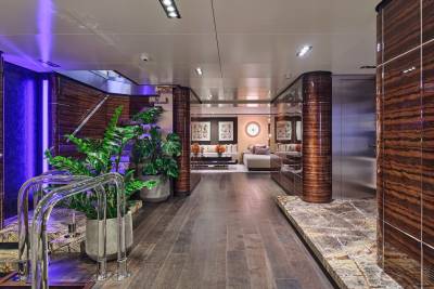 A luxurious yacht interior features a spa-like area with lush plants in the foreground and a modern living room with artwork in the background.