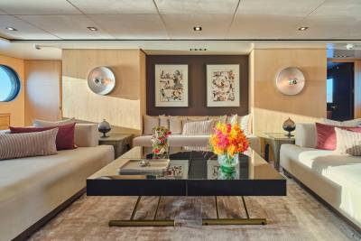 A modern yacht lounge features a sleek coffee table with a vibrant floral arrangement in the foreground, while the background reveals comfortable seating and artwork on wood-paneled walls.