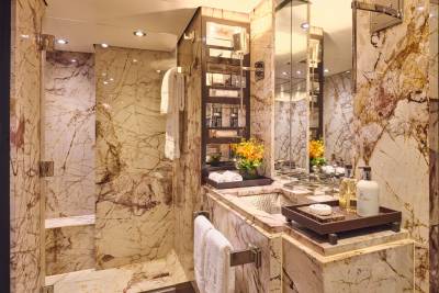 A luxurious bathroom with marble walls and a sink area in the foreground, and a shower stall in the background.