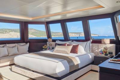 A luxurious bedroom with a large bed and sofa in the foreground is set against a backdrop of a scenic coastal view through large windows.
