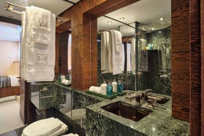 A luxurious bathroom with a marble countertop and sink in the foreground, and a bedroom visible in the background through a doorway.