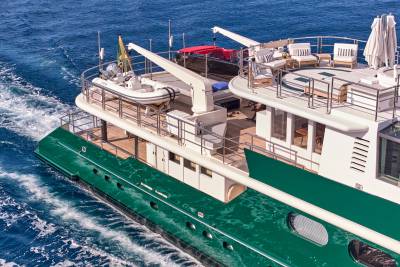A green yacht with a tender boat on its deck cruises through blue ocean waters.
