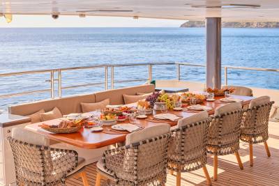 A beautifully set dining table laden with food on a yacht's deck overlooks a calm, blue ocean.
