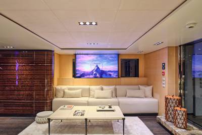 A modern living room with a large sectional sofa and coffee table in the foreground, and a projector screen displaying the Paramount Pictures logo in the background.