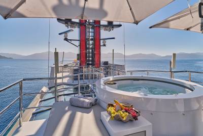 A luxurious hot tub and lounge chair sit on the deck of a yacht, with a vast ocean and distant mountains in the background.