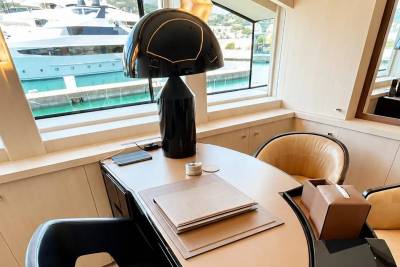 A sleek black lamp sits on a desk with a yacht visible through the window in the background.