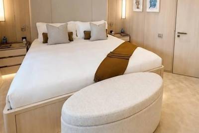 A plush white bed with a brown throw is in the foreground, while the background features wood-paneled walls and two framed pictures.