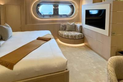 A luxurious yacht bedroom features a large bed in the foreground and a curved window with a view of the ocean in the background.