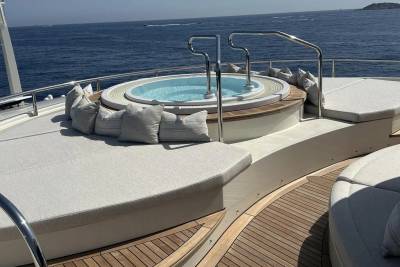 A circular jacuzzi with plush cushions sits on the deck of a yacht, with the calm blue ocean stretching to the horizon in the background.