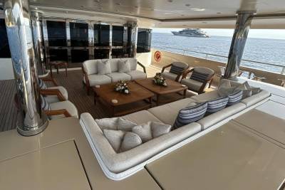 A luxurious yacht deck with plush seating in the foreground and another yacht on the ocean in the background.