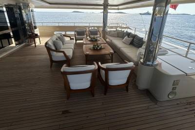 Plush white seating arrangements on a wooden deck are set against a backdrop of the calm sea and distant islands.