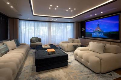 Plush cream sofas and a dark blue ottoman fill the foreground of a home theater, while a large screen displays the Disney castle in the background.