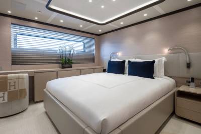 A luxurious yacht bedroom with a large bed in the foreground and a window with blinds in the background.