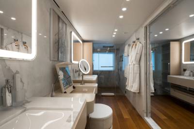 A modern bathroom with a vanity and sinks in the foreground and a glass-enclosed shower and another sink in the background.