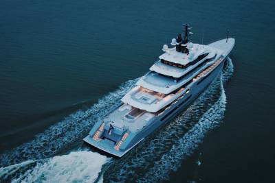 A luxurious yacht cruises through calm, dark water, leaving a foamy wake behind it.