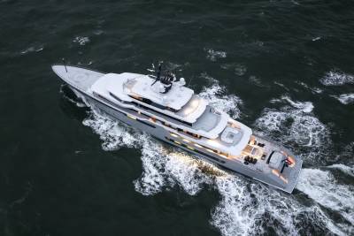 A large, modern yacht cruises through choppy, dark water, leaving a white wake behind it.