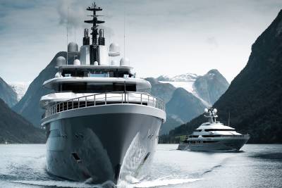 A large, modern yacht dominates the foreground, with another yacht trailing behind it in a serene, mountainous fjord.