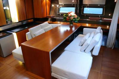 A long, polished wooden table with white sofas on either side is set against a background of dark wood paneling and windows on a yacht.