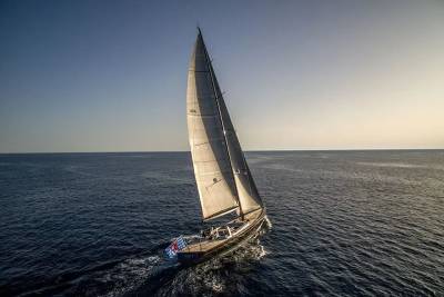 A sleek sailboat with full sails cuts through the deep blue ocean under a clear, bright sky.
