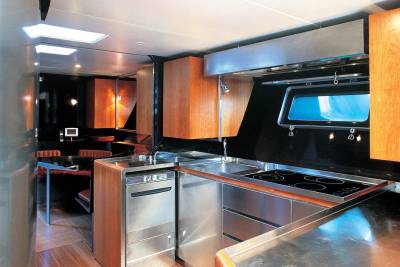 A modern, stainless steel kitchen with wooden cabinets in the foreground is contrasted by a dimly lit dining area with warm lighting in the background.