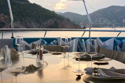 A set dining table on a yacht's deck overlooks a tranquil sea and a lush, mountainous coastline.