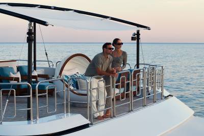 A couple stands on the deck of a luxurious yacht, gazing out at the calm ocean under a soft sky.