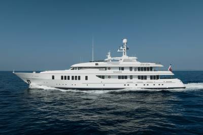 A large white yacht cruises through calm blue water with a clear blue sky in the background.