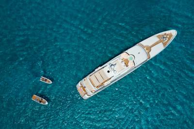 A large white yacht floats on a turquoise sea, with two smaller boats nearby.