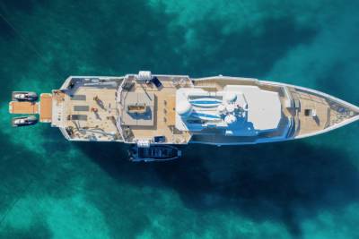 A luxurious yacht with people on its deck floats on the clear turquoise water.