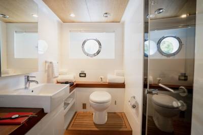 A modern bathroom with a white sink and wooden accents in the foreground, and porthole windows looking out to greenery in the background.
