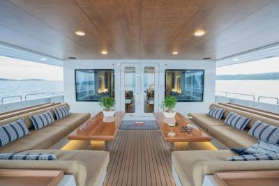 Luxurious outdoor seating with plush cushions and wooden tables fills the foreground, while the background reveals a serene ocean view with distant islands under a bright sky.