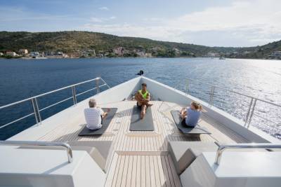 Three people practice yoga on the deck of a yacht with a coastal town in the background.