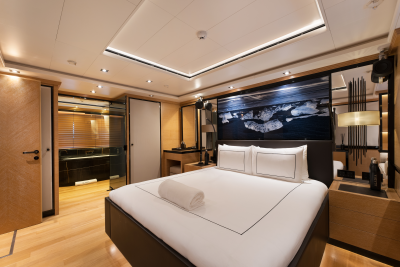 A luxurious bedroom with a neatly made bed in the foreground and a modern bathroom visible through an open doorway in the background.