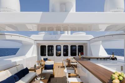 A luxurious yacht deck with a seating area and bar in the foreground overlooks the calm blue ocean in the background.