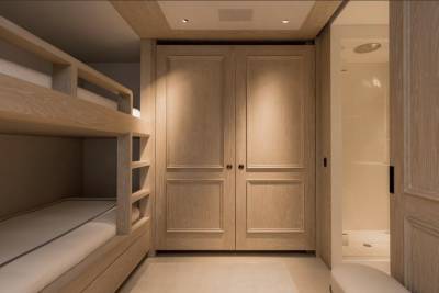 A bunk bed with white mattresses is in the foreground, while a closet with double doors and a shower stall are in the background.