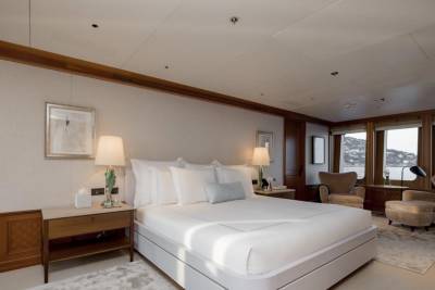 A luxurious bedroom with a large bed in the foreground and windows overlooking a coastal town in the background.