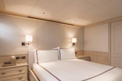 A neatly made bed with white linens and purple trim sits in the foreground, while a wooden door and wall paneling form the background.