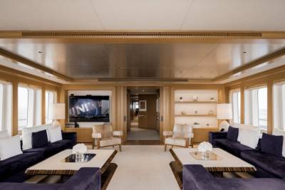 Plush purple sofas and modern coffee tables fill the foreground of a luxurious yacht lounge, while a hallway with doors and shelves stretches into the background.