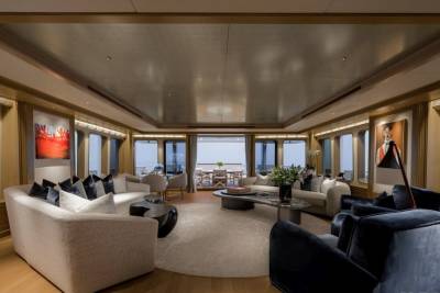 Plush sofas and modern art adorn the spacious, well-lit living area of a yacht, with large windows offering a glimpse of the ocean and distant horizon.