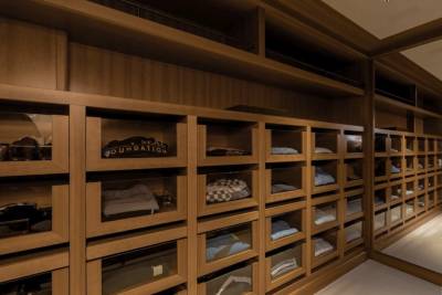 A well-organized walk-in closet with wooden shelves filled with folded clothes in the foreground, and a mirrored wall reflecting the closet's interior in the background.