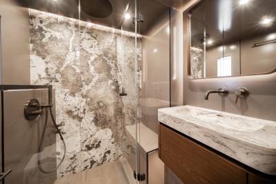 A modern bathroom features a marble-clad shower in the foreground and a vanity with a matching sink and a large mirror in the background.