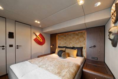 A luxurious bedroom features a plush bed with decorative pillows in the foreground, while tribal masks adorn the wall in the background.