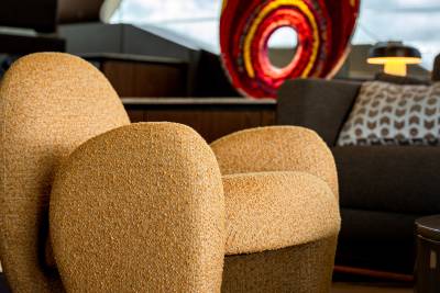 A textured, mustard-yellow armchair sits in the foreground, with a dark sofa and a colorful abstract sculpture visible in the background.