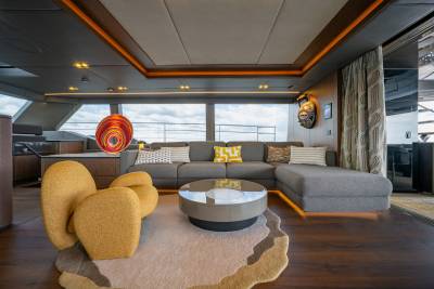 A modern living area with plush yellow armchairs and a sectional sofa in the foreground, and large windows offering a view of the sky and water in the background.
