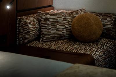 A cozy seating area with patterned cushions and a round textured pillow is illuminated by a spotlight against a dark wooden background.