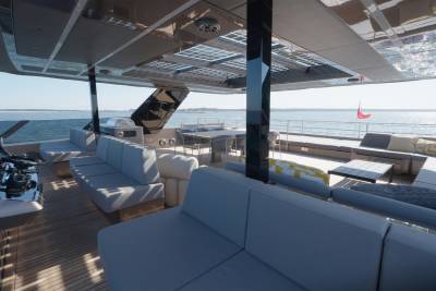 Plush grey seating arrangements fill the foreground of a modern yacht's deck, while the background reveals a calm ocean under a clear sky.
