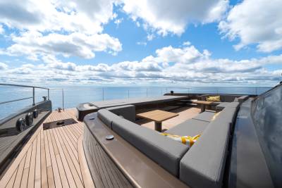 A luxurious yacht deck with plush seating in the foreground overlooks a calm ocean under a cloudy blue sky in the background.