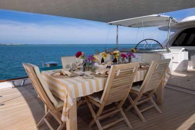 A beautifully set dining table with floral arrangements on a yacht's deck overlooks a calm blue ocean under a clear sky.