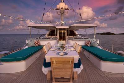 A beautifully set dining table on a yacht's deck is illuminated by string lights against a twilight sky.