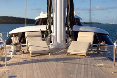 Two lounge chairs sit on the wooden deck of a yacht in the foreground, with the calm blue ocean and distant green islands visible in the background.